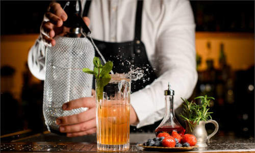 Barman che versa liquido su un cocktail usando una bottiglia Dash