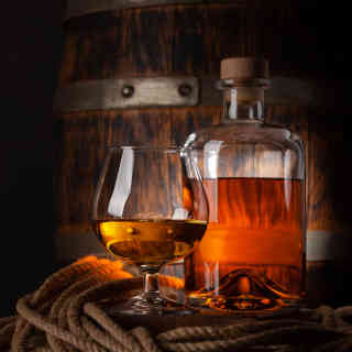 A glass and a bottle of rum in front of a barrel