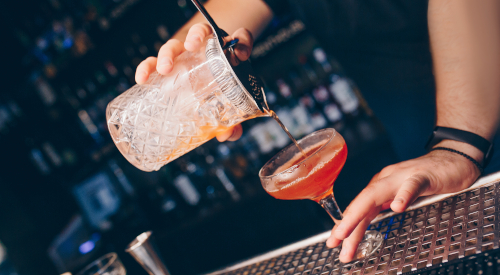 Un barman usa uno strainer per versare liquido filtrato in un bicchiere da cocktail