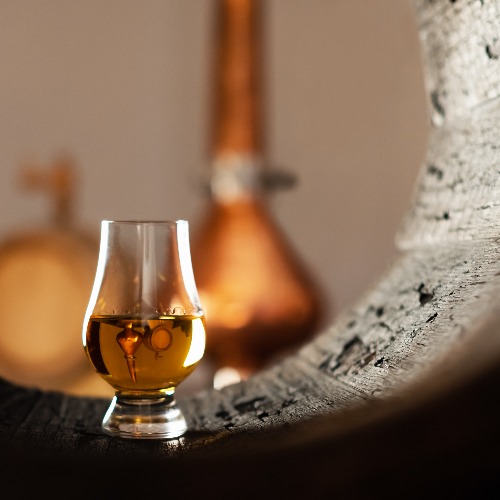 A glass of brandy in an old oak barrel. Copper still on a black background. Traditional alcohol distillery concept.