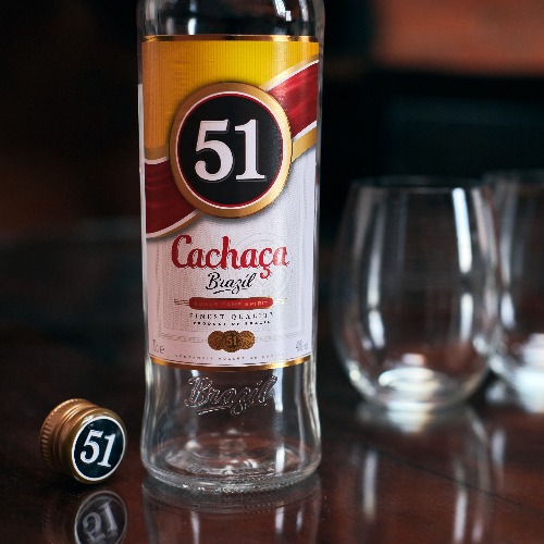 Cachaca 51 bottle with two glasses. Brazilian rum. Exotic Brazil strong alcohol drink from fermented sugarcane juice. Loft apartment background.