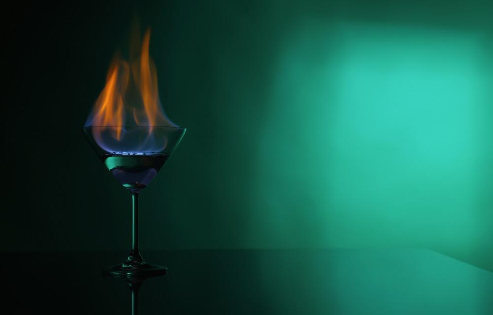 Cocktail glass with flaming vodka on a green background.