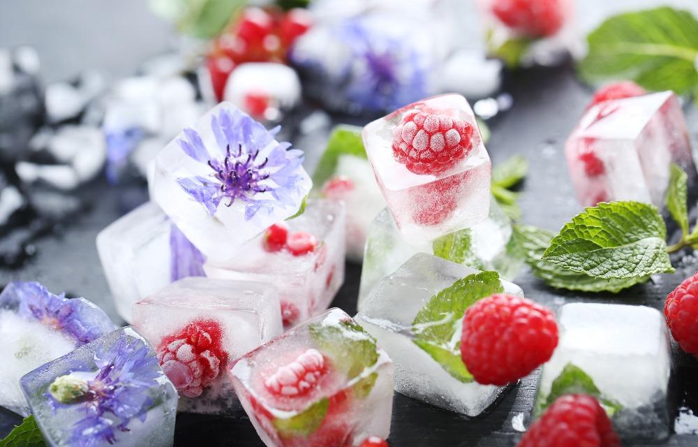 Cubos de hielo con frambuesas y hojas de menta en una mesa de madera.