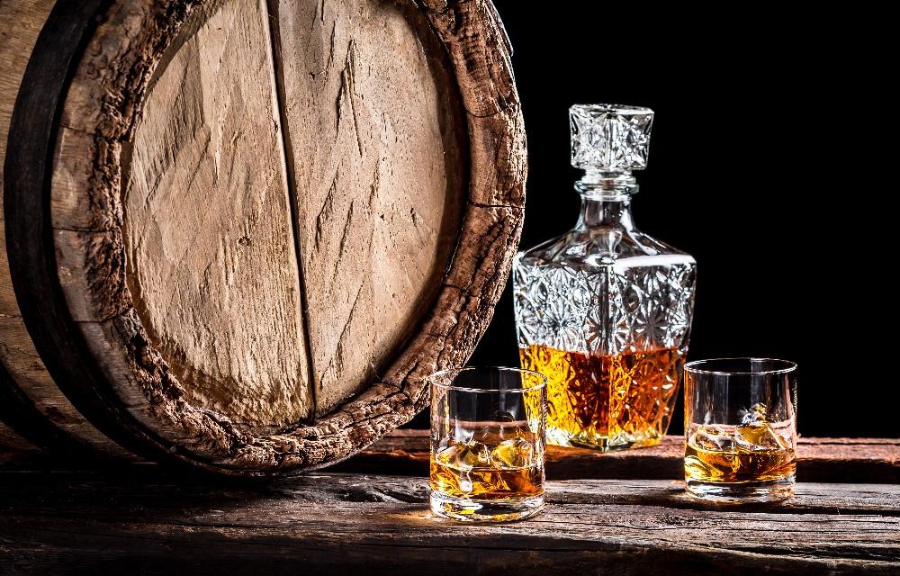 Bottiglia di whisky in cristallo, bicchiere di whisky e piccola botte di legno.