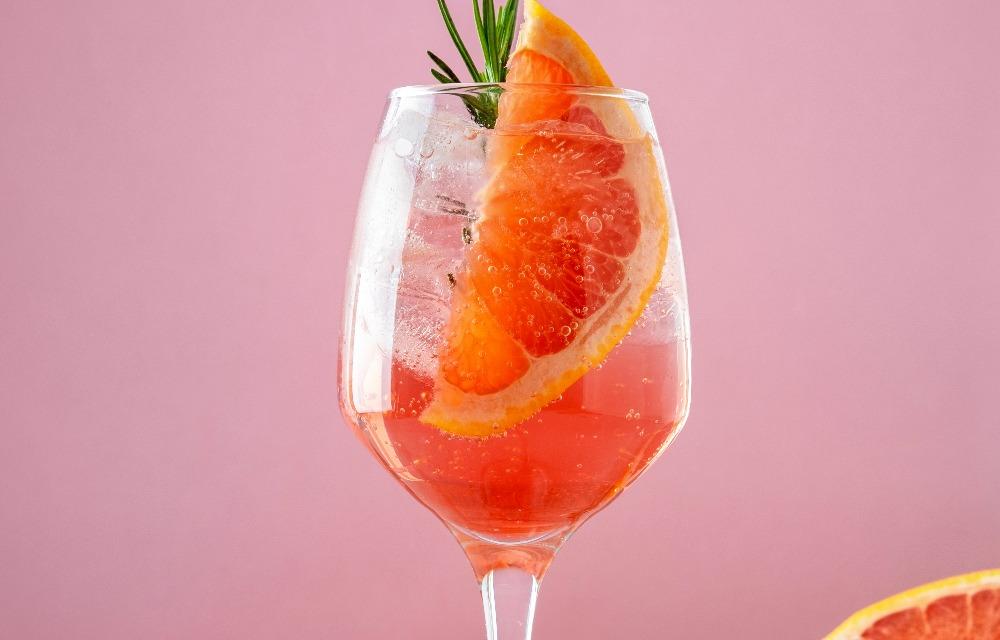 cocktail spritz aperol sur un fond rose avec des rondelles d'oranges