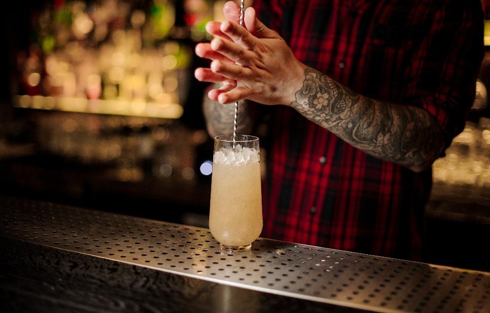 Un barista mescola un cocktail Trinidad Swizzle con il cucchiaio nel bicchiere sul bancone del bar.