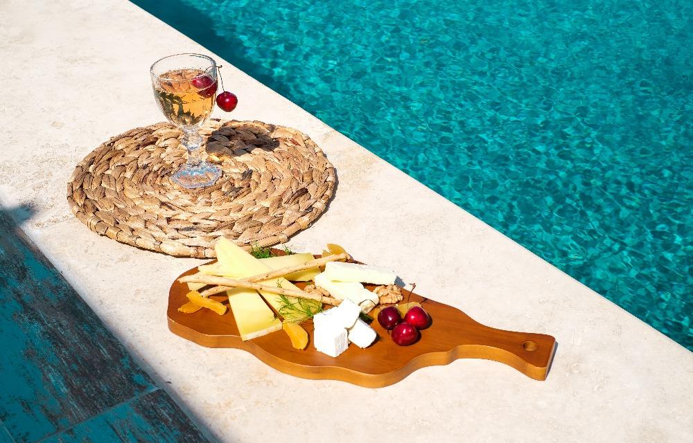 Un bicchiere di cocktail e un vassoio di formaggi ai bordi della piscina. Piatto di formaggio per cocktail servito su un vassoio di legno e vimini ai bordi della piscina.