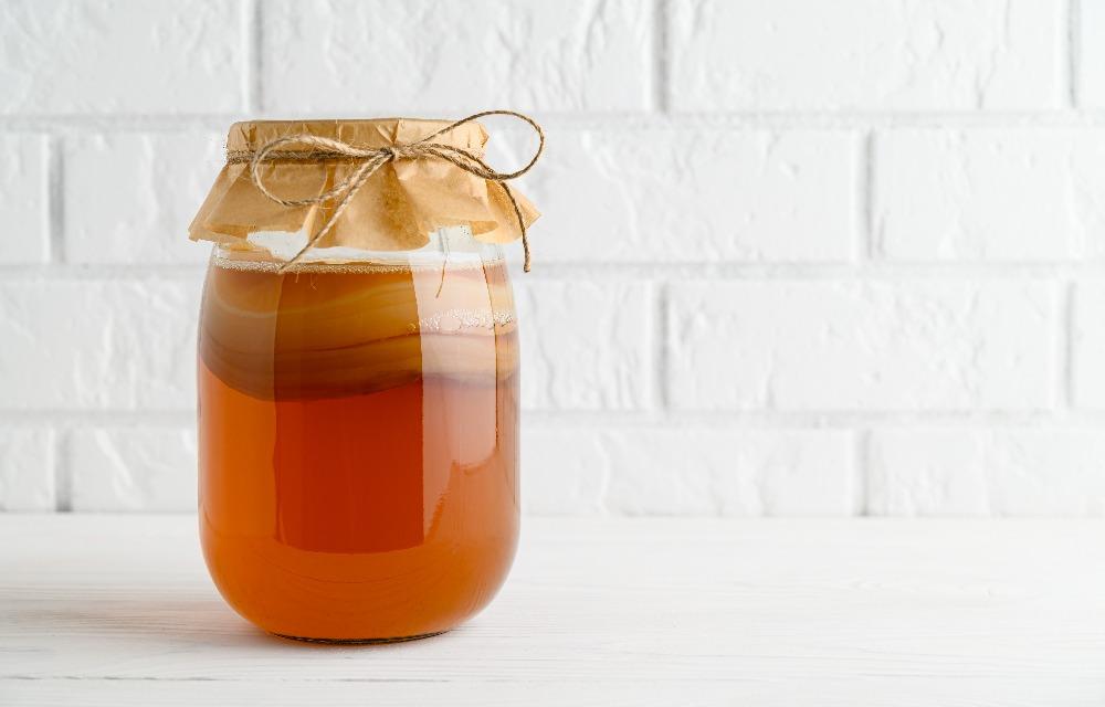 A transparent pitcher of kombucha on a white table with its white background.